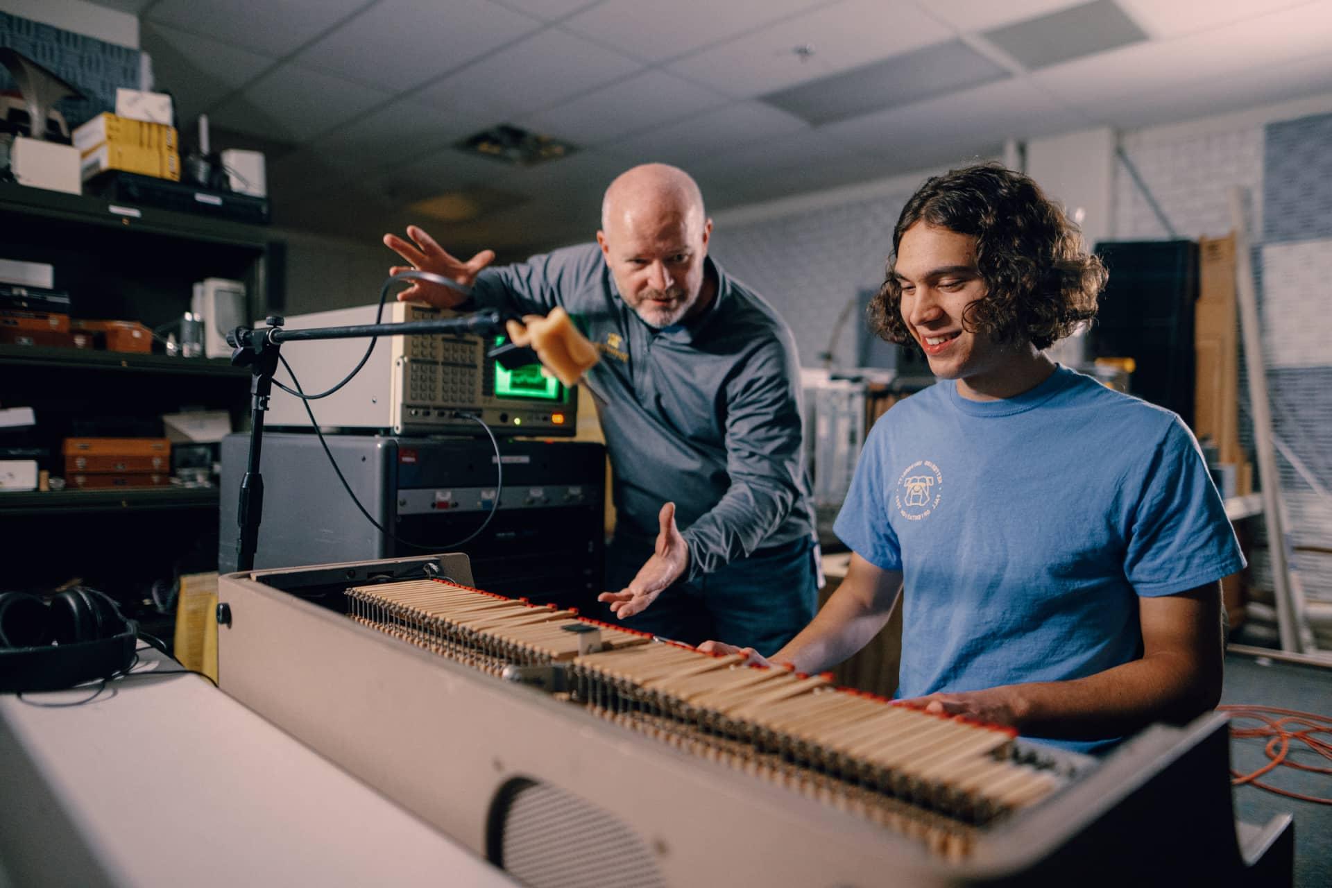 A Kettering student plays an electronic keyboard in the Acoustic Lab. A professor listens and gestures with his hands.