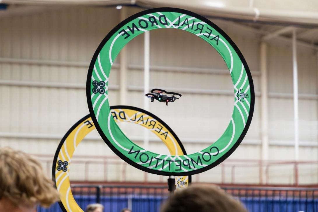 A drone flies through a green ring, with a yellow ring beyond it.